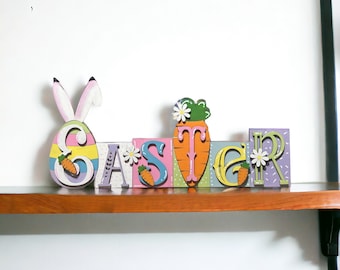 May include: Wooden Easter sign with the word "Easter" spelled out in colorful blocks. Each letter is decorated with a different Easter theme, including a bunny, eggs, carrots, and flowers.