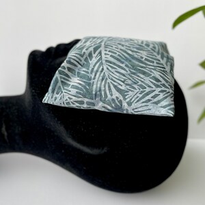 May include: A gray and white patterned fabric pouch with a leaf design. The pouch is sitting on a black surface.