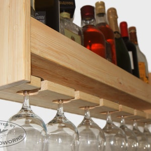 May include: A wooden wine rack with a shelf for bottles and a lower rack for hanging wine glasses. The rack is made of natural wood and has a rustic look. The rack is handcrafted by Samp Woodworks.
