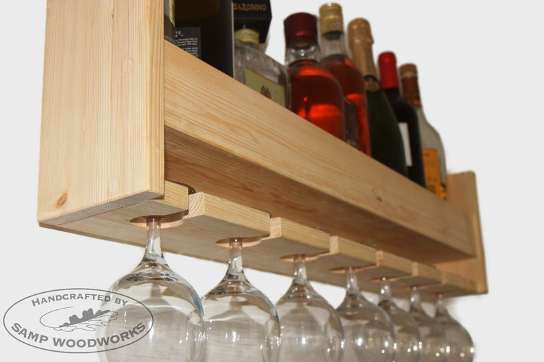 May include: A wooden wine rack with a shelf for bottles and a lower rack for hanging wine glasses. The rack is made of natural wood and has a rustic look. The rack is handcrafted by Samp Woodworks.