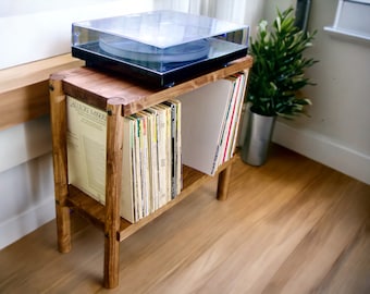 May include: A wooden record player stand with two shelves for storing vinyl records. The stand is stained a dark brown color and has a turntable on the top shelf. The stand is in a room with wood floors.