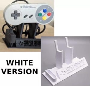 May include: A grey Super Nintendo controller on a black stand, with the words "SUPER NINTENDO". A white stand is also shown, with the same text, and the words "WHITE VERSION". The controller has coloured buttons.