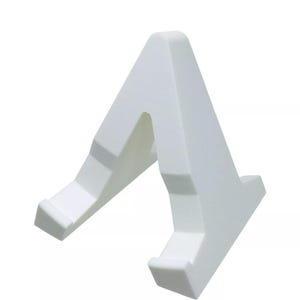 May include: A white, angled display stand. The stand has a triangular shape with a cutout in the center and two angled supports at the base. The supports have a small lip to hold an item. The stand is made of a solid, opaque material.