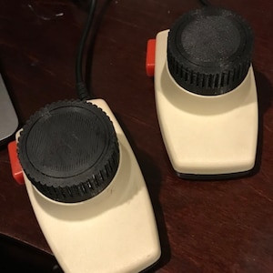 May include: Two vintage computer mice with a cream-colored body, black top dial, and a red button. The mice are connected by a black cable. The design is retro and classic, suitable for collectors or enthusiasts of vintage technology.