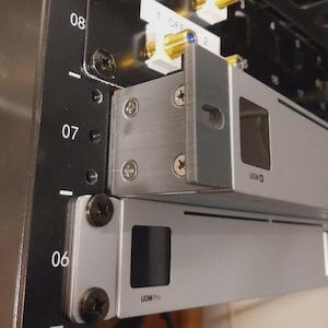 Puede incluir: Primer plano de un rack de servidor con componentes de metal plateado. El rack tiene etiquetas numeradas y los textos "USW" y "UDM Pro" son visibles. Los tornillos aseguran los componentes, mostrando un diseño estructurado.