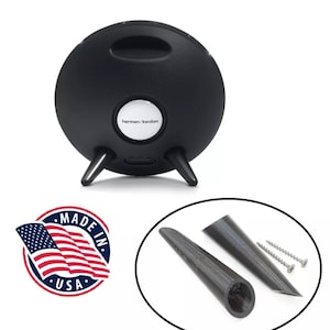 Op de afbeelding: Zwarte Harman Kardon-luidspreker met drie poten en een handvat. De luidspreker heeft een witte knop met de merknaam. Ook inbegrepen zijn twee zwarte luidsprekerstandaards en twee schroeven. Een "Made in USA"-sticker is ook inbegrepen.