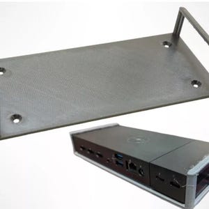 May include: A gray, 3D-printed docking station mount and a black docking station. The mount has a rectangular base with two raised sides and pre-drilled holes for mounting. The docking station has multiple ports.