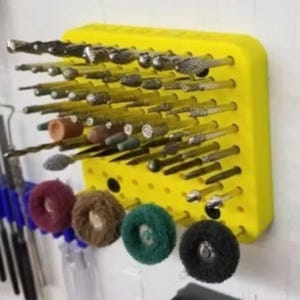 Puede incluir: Un organizador de herramientas amarillo lleno de varias brocas para herramientas rotativas. Las brocas son de diferentes formas y tamaños, incluyendo cilíndricas, cónicas y esféricas. Debajo, cinco ruedas de pulido de colores: burdeos, marrón, verde y negro.