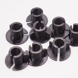 May include: A collection of seven small, black, cylindrical plastic parts. Each part has a circular base with a central opening and a vertical, open-ended cylinder rising from the center. The parts are arranged on a white surface.