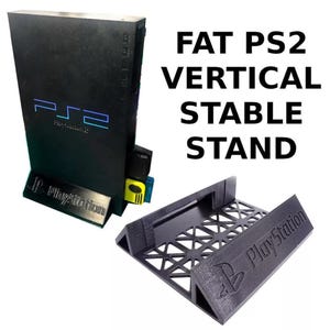 Peut inclure: Support vertical noir pour console Fat PS2. Le support porte l'inscription "FAT PS2 VERTICAL STABLE STAND". Il est conçu pour maintenir la console à la verticale. Comprend une base séparée avec le logo PlayStation.
