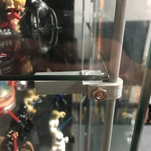 May include: A gray 3D-printed shelf support system with a metal rod and a glass shelf. The support system is attached to the glass shelf with a bolt. The shelf is holding various figurines.