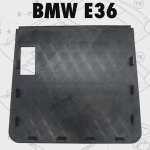 Puede incluir: Una pieza de automóvil negra con el texto "BMW E36" en la parte superior. La pieza tiene forma rectangular con un recorte cuadrado y varias pestañas rectangulares. La superficie tiene un patrón texturizado.