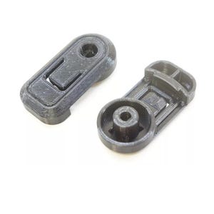 May include: Two black 3D-printed plastic components. One is rectangular with a recessed area and a hole. The other is a circular base with a central hole and a rectangular section. Both have a textured surface.