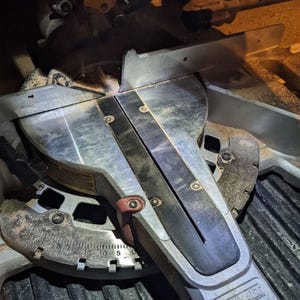May include: A close-up of a DeWalt miter saw. The saw features a silver blade, a black and silver base, and a red lever. The saw has a degree scale for precise angle cuts. Sawdust is visible on the surface.