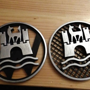 Peut inclure: Deux emblèmes métalliques circulaires représentant un château avec un cerf au sommet. L'un a un fond noir uni avec la lettre "V" incorporée, l'autre a un fond en treillis.