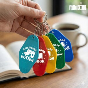 May include: A set of five colorful keychains with the words "Cats Books Coffee", "Book", and "Reading" printed on them. The keychains are in teal, red, yellow, green, and blue. The keychains are attached to a silver keyring.