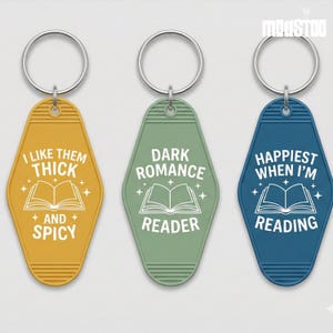 May include: Three keychains with silver rings. The keychains are in yellow, green, and blue. Each keychain has a different text: "I LIKE THEM THICK + AND + SPICY", "DARK ROMANCE READER", and "HAPPIEST WHEN I'M READING". Each keychain has a book graphic.
