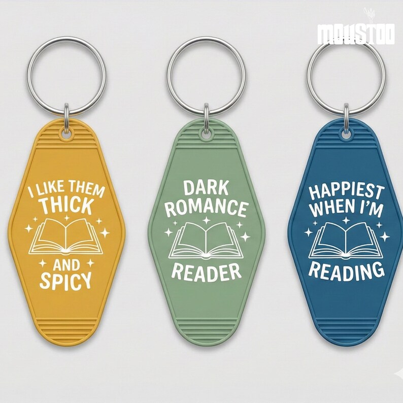 May include: Three keychains with silver rings. The keychains are in yellow, green, and blue. Each keychain has a different text: "I LIKE THEM THICK + AND + SPICY", "DARK ROMANCE READER", and "HAPPIEST WHEN I'M READING". Each keychain has a book graphic.