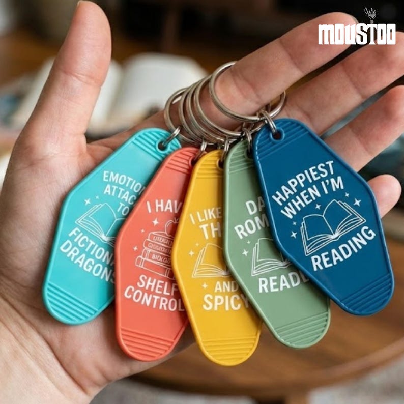 May include: A set of five colorful keychains with silver rings. Each keychain has a different color and a unique book-themed quote in white text. The keychains are teal, red, yellow, green, and blue.
