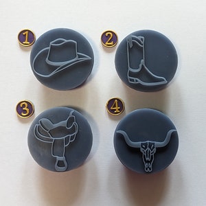 May include: Four gray round rubber stamps with different western themed designs. The designs are a cowboy hat, a cowboy boot, a saddle, and a bull skull. Each stamp has a gold number on a purple circle next to it.