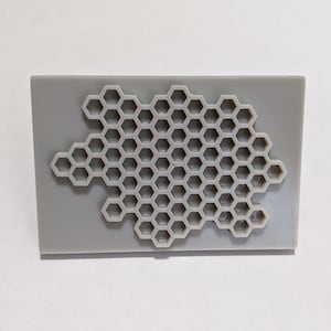 May include: A gray plastic mold with a honeycomb pattern. The mold is rectangular and has a raised honeycomb design.