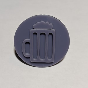 May include: A purple, round, 3D printed stamp with a raised design of a beer mug with foam on top.