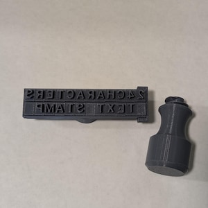 May include: A black plastic text stamp with the words "TEXT STAMP 24 CHARACTERS" on it. The stamp is attached to a black plastic handle.