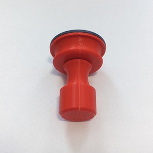 May include: A red plastic knob with a blue ring on top. The knob has a cylindrical shape with a rounded top and bottom.