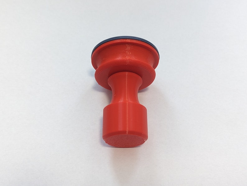 May include: A red plastic knob with a blue ring on top. The knob has a cylindrical shape with a rounded top and bottom.