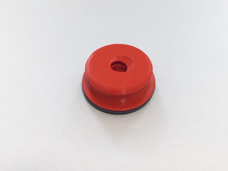 May include: A red plastic cap with a black ring around the bottom. The cap has a small hole in the center.