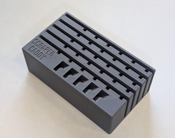 May include: A grey plastic scraper caddy with the words "SCRAPER CADDY" embossed on the side. The caddy has multiple slots for holding scrapers and a series of horizontal grooves on top.