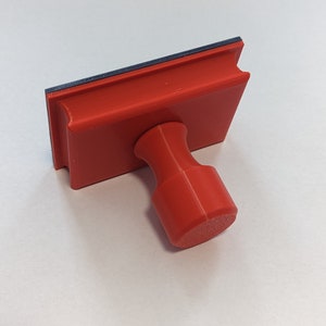 May include: A red rubber stamp with a black ink pad and a red plastic handle.