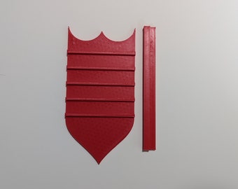 May include: A red, shield-shaped object with a textured surface and a decorative top, alongside a matching rectangular piece. The shield has horizontal lines and a pointed bottom. The objects are likely components of a larger item.
