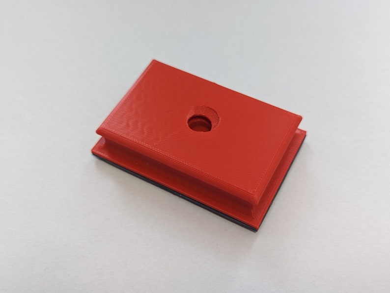 May include: A red plastic block with a round hole in the center. The block has a black border around the edges.