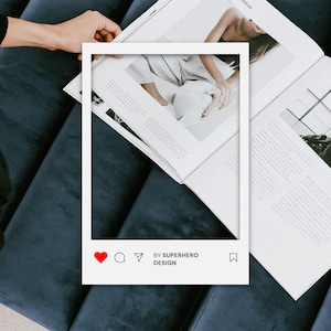 May include: A white rectangular social media frame overlay featuring a red heart icon, comment bubble, paper airplane, and bookmark icon. The text BY SUPERHERO DESIGN is printed in black at the bottom of the frame, which is positioned over an open magazine.
