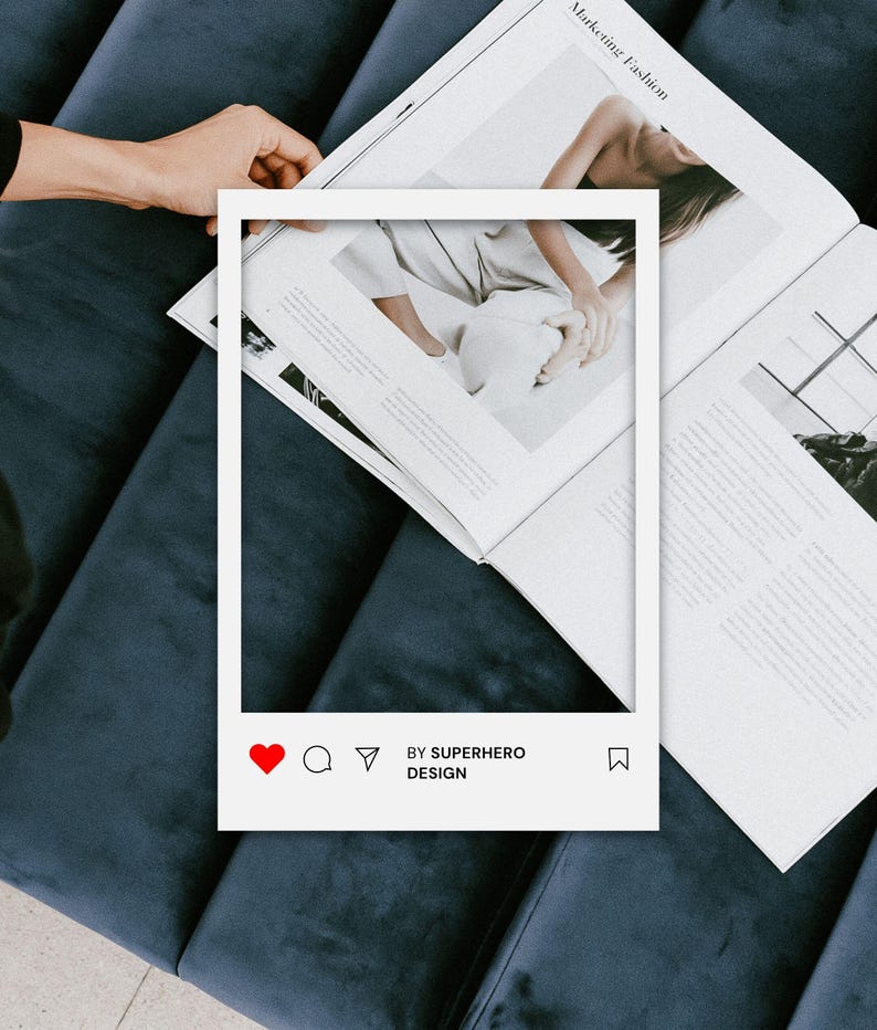 May include: A white rectangular social media frame overlay featuring a red heart icon, comment bubble, paper airplane, and bookmark icon. The text BY SUPERHERO DESIGN is printed in black at the bottom of the frame, which is positioned over an open magazine.