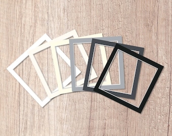 May include: A set of eight picture frames in various sizes and colors, including white, cream, gray, and black. The frames are arranged in a fan shape on a wooden surface.