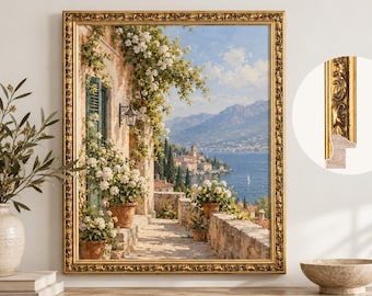 May include: A framed landscape painting depicting a Mediterranean terrace with terracotta pots, white flowers, and green shutters overlooking a blue lake and mountains. The frame is ornate, gold-colored, and features a detailed relief pattern.