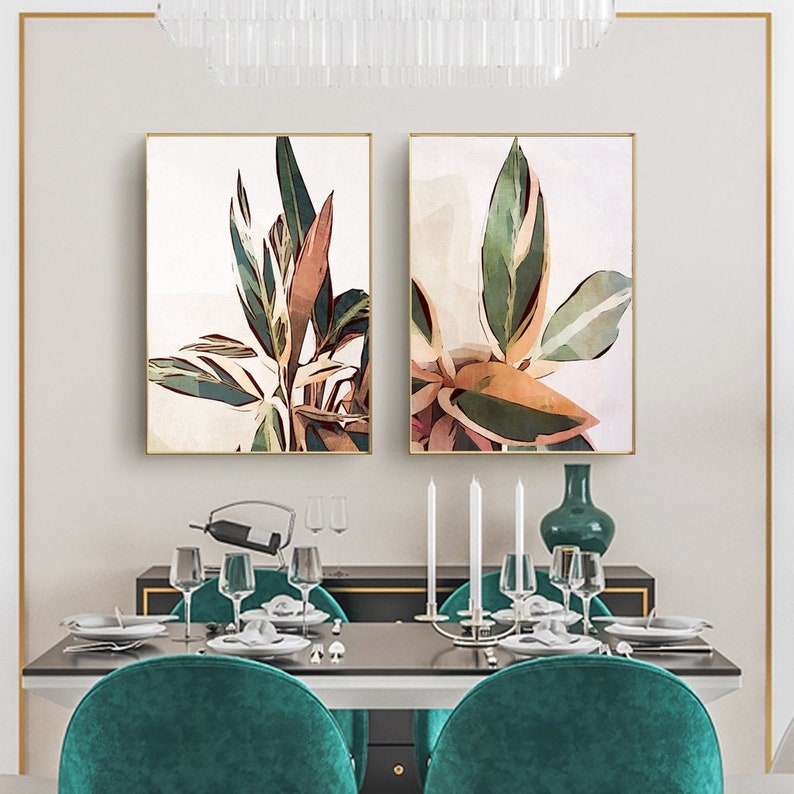 May include: Two framed watercolor paintings of green and brown tropical leaves with white accents. The paintings are hanging on a white wall above a dining table with green chairs.