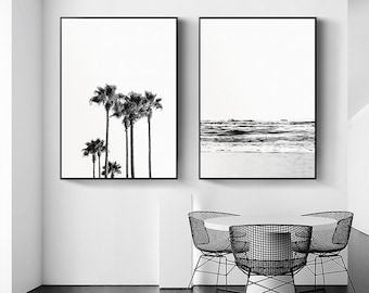 May include: Two black and white framed prints. The print on the left shows a group of palm trees against a white background. The print on the right shows a black and white image of the ocean with waves crashing on the shore.