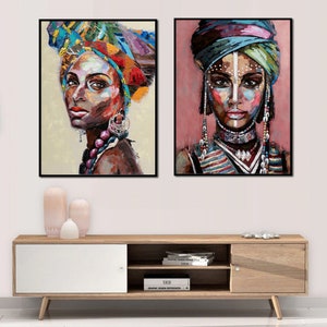 May include: Two colorful paintings of women wearing head wraps and traditional jewelry. The paintings are framed in black and set against a white wall.