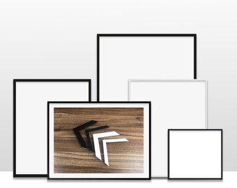 May include: Four black picture frames of different sizes, with one frame containing a photo of a wooden surface with three black and white geometric shapes.