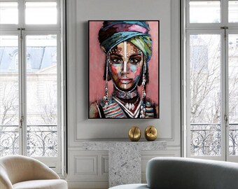 May include: A framed portrait of a person with a colorful head wrap and face paint. The artwork features a pink background and the person is adorned with beaded jewelry. The painting is displayed in a well-lit room with large windows and modern furniture.