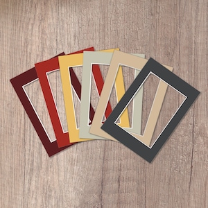 May include: A set of seven different coloured mount boards, each with a white core and a rectangular opening. The mount boards are arranged in a fan shape, with the darkest colour at the bottom and the lightest colour at the top.