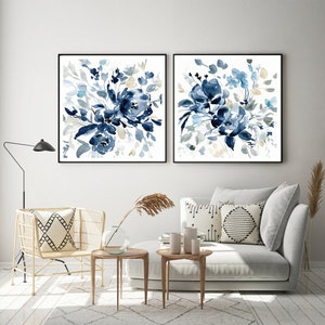 May include: Two framed watercolor paintings of blue floral bouquets on a white background. The paintings are hanging on a white wall above a gray couch and a gold chair.