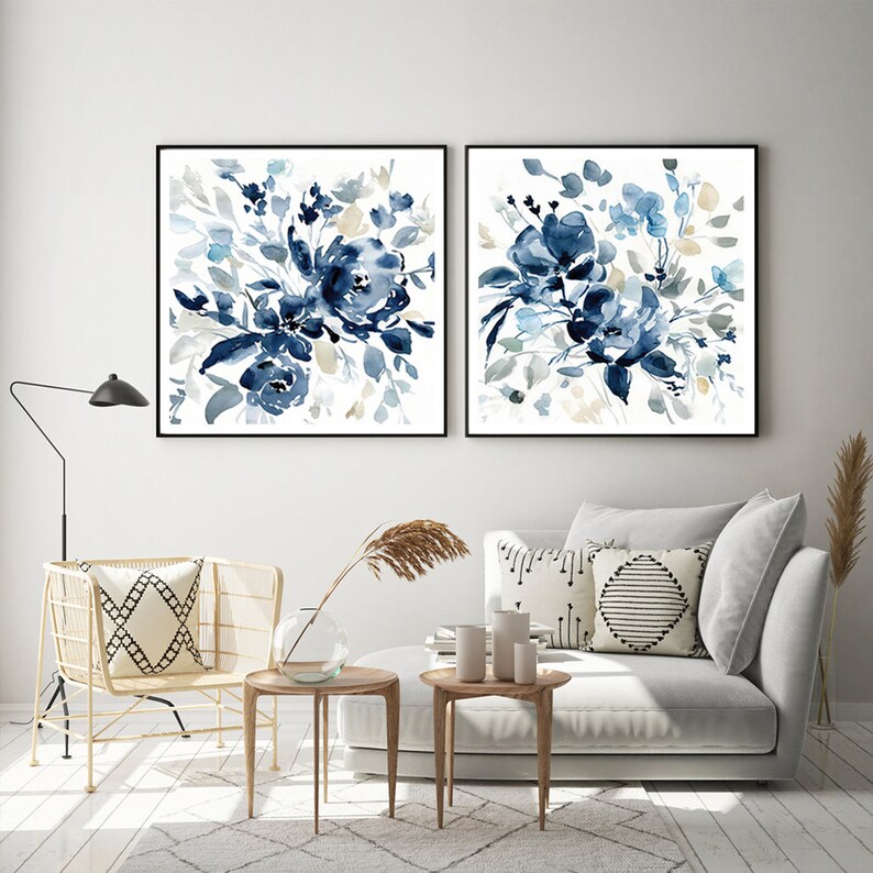 May include: Two framed watercolor paintings of blue floral bouquets on a white background. The paintings are hanging on a white wall above a gray couch and a gold chair.