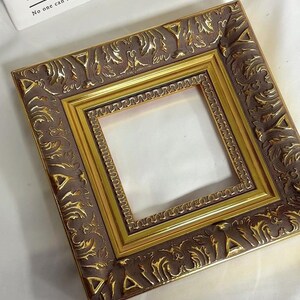 May include: A gold and brown ornate picture frame with a decorative design. The frame is empty and ready to display a photo or artwork.