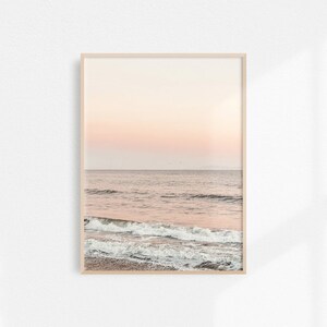May include: A photograph of a seascape with a pink and orange sunset over the ocean. The waves are crashing on the shore, and the water is a light blue color.
