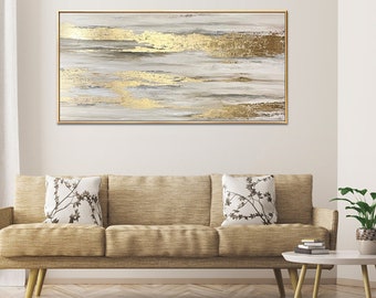 May include: Abstract painting with gold leaf accents on a white canvas. The painting is framed in a thin gold frame and is hanging on a white wall above a brown couch.