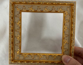 May include: A gold picture frame with an ornate design. The frame has a light brown background with gold accents.